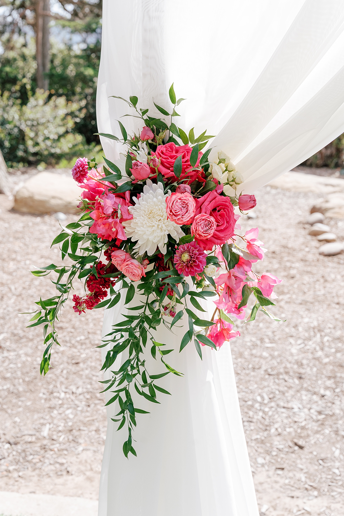 Vignette of a tropical wedding ceremony site's arch covered in white fabric and bright pink flowers| Image by San Diego Wedding Photographer Hope Helmuth