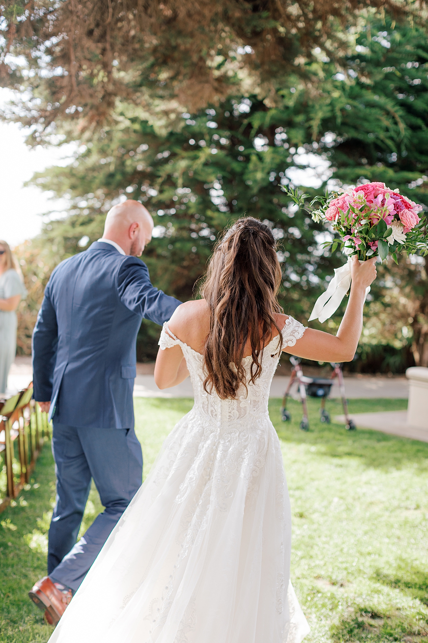 Bride and groom holding hands while walking away from the camera while bride holds bouquet in the air | Image by Hope Helmuth Photography