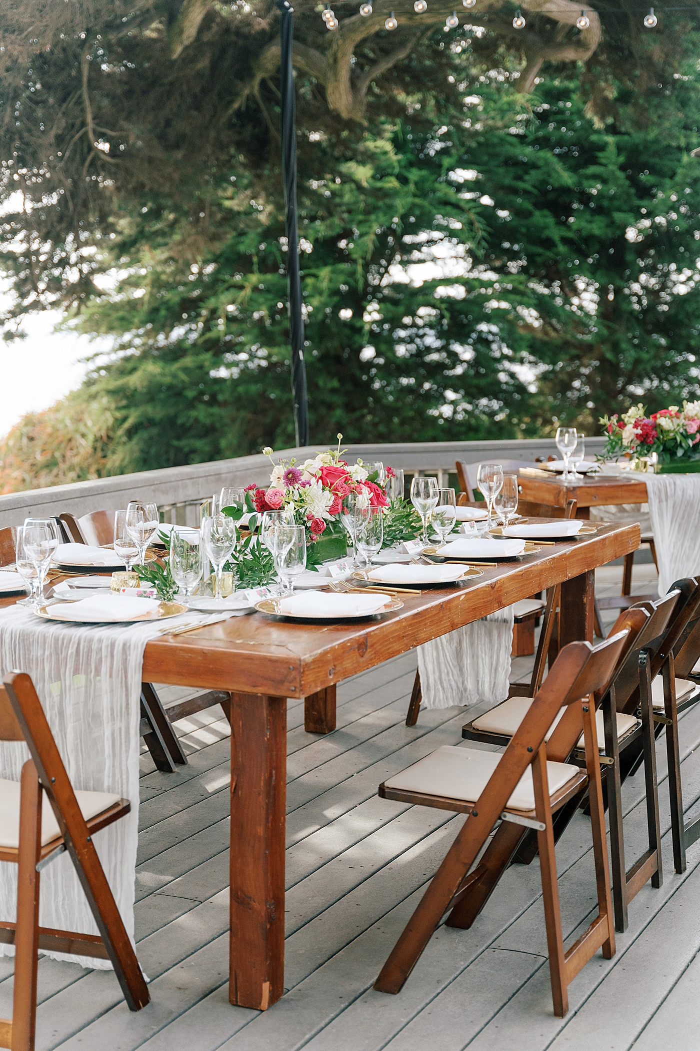 Detail of a wooden wedding dinner table with wooden folding chairs and white table runner | Image by San Diego Wedding Photographer Hope Helmuth