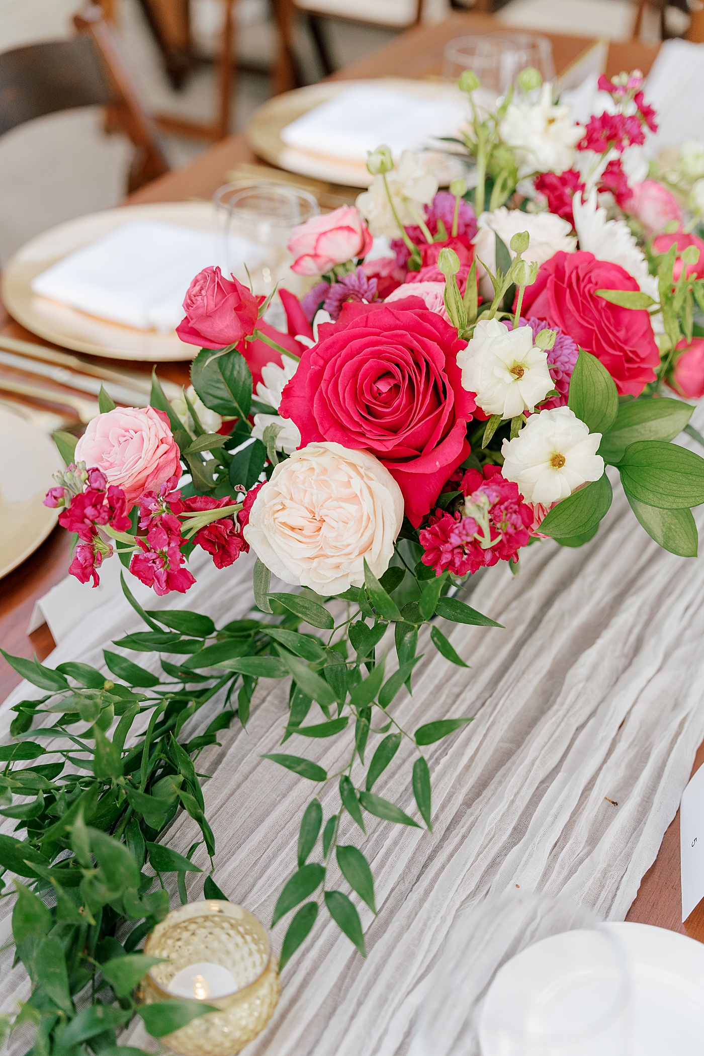 Detail of a wooden wedding dinner table with a white table runner, greenery, and a bright floral centerpiece | Image by San Diego Wedding Photographer Hope Helmuth