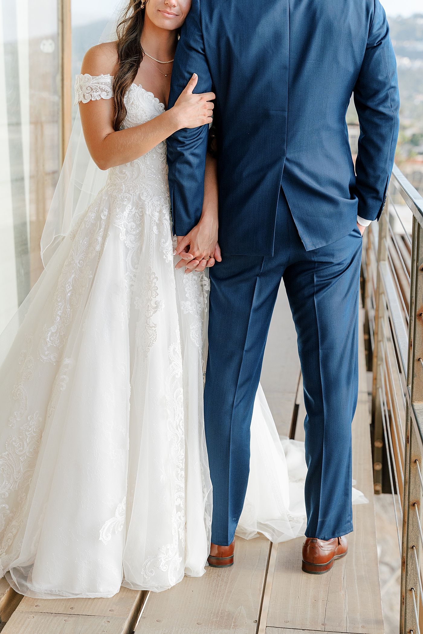 Vignette of a groom in navy suit and bride in wedding dress holding hands. The bride is facing the camera with her head on the shoulder of the groom who is facing away from the camera | Image by San Diego Wedding Photographer Hope Helmuth