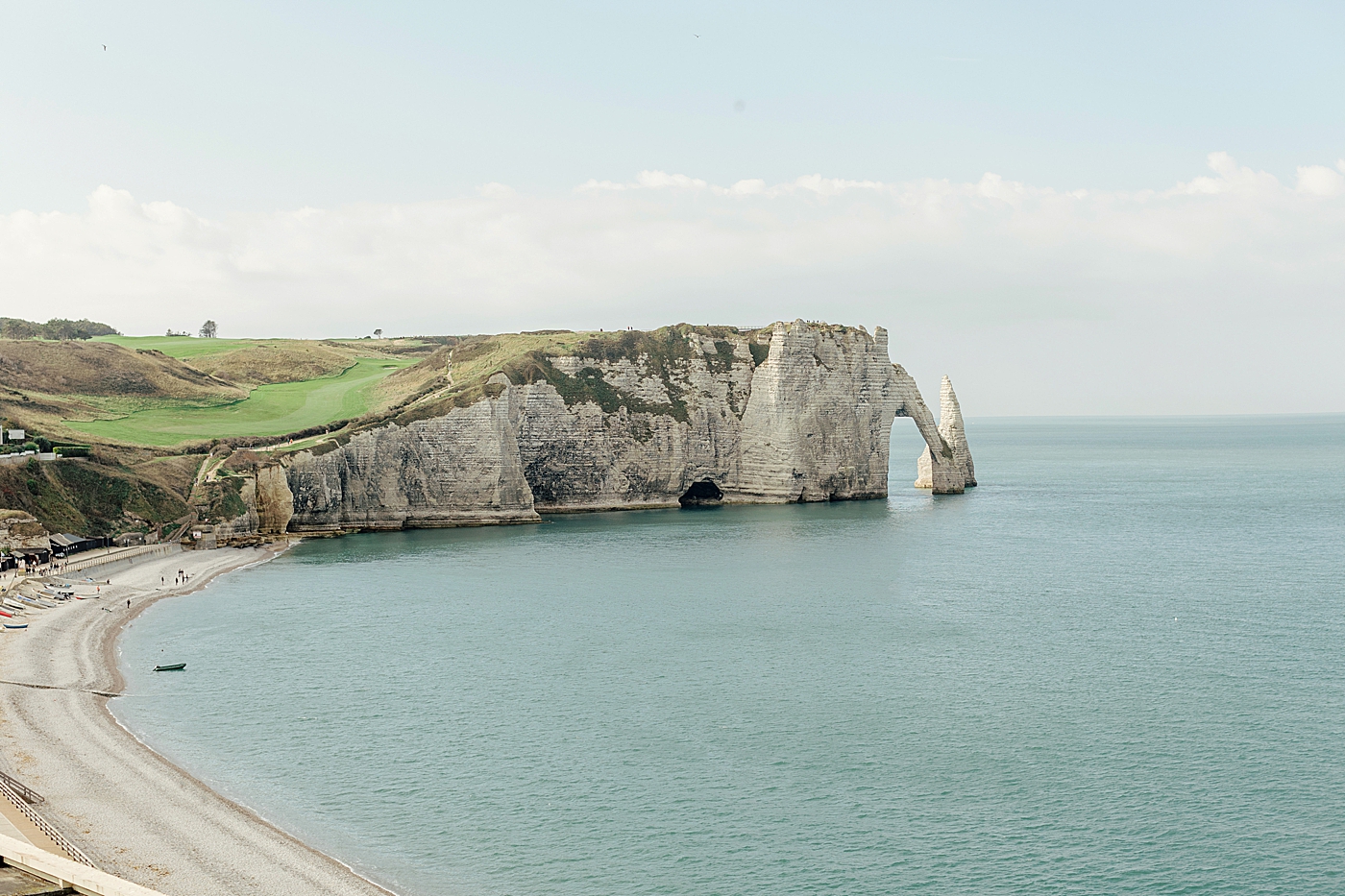 View of an empty French beach with cliffs in the back ground, calm water, and boats sitting on shore during a trip with France Wedding Photographer Hope Helmuth Photography