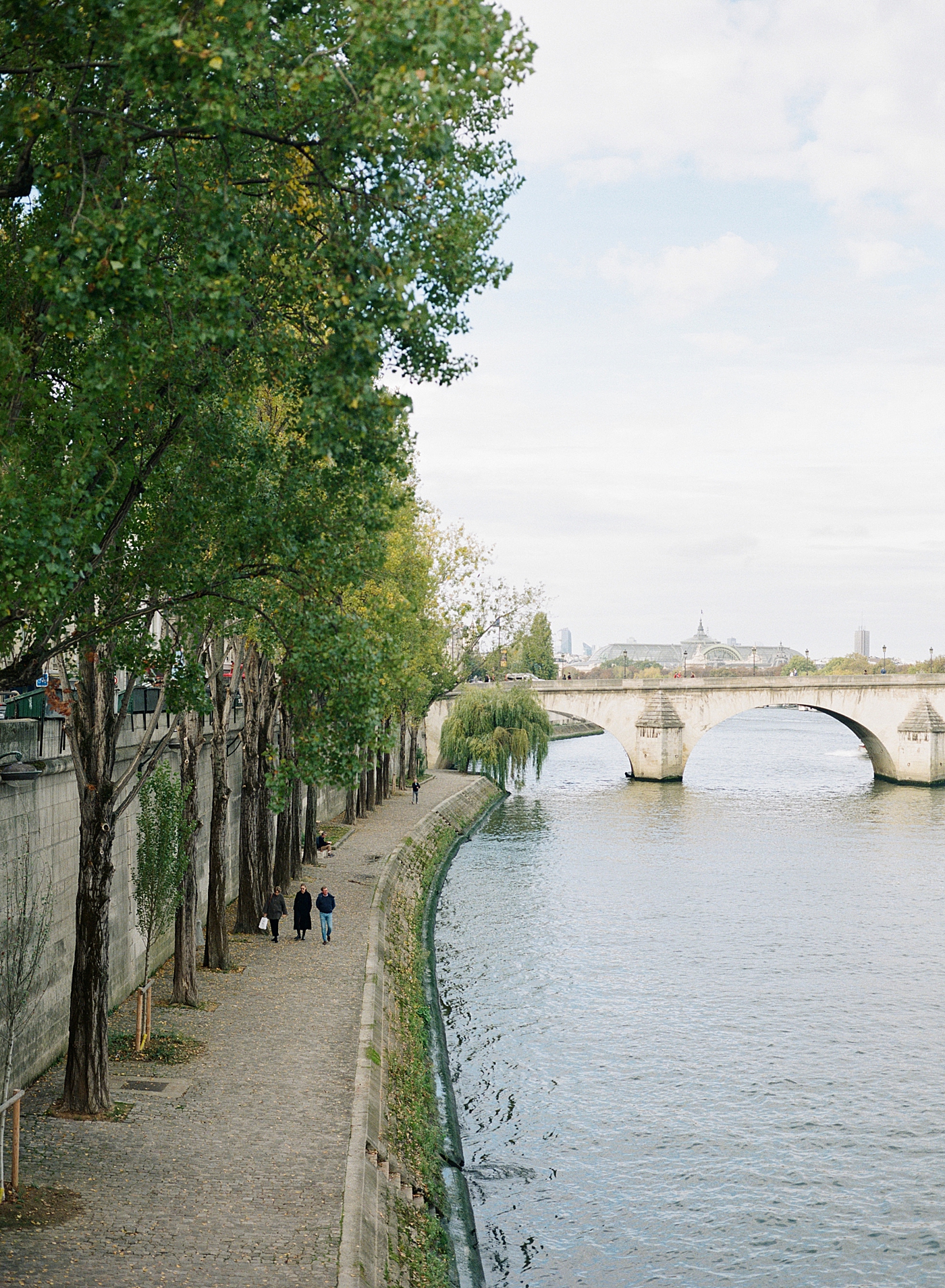 Three people walking next to a French canal with a bridge in the background during a trip with France Wedding Photographer Hope Helmuth Photography