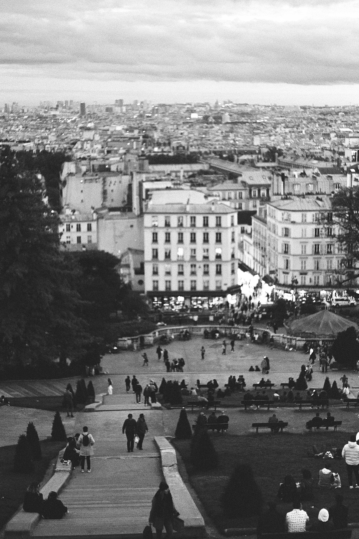 Black and white photo looking over the vast city of Paris from the top a hill with passersby below during a trip with France Wedding Photographer Hope Helmuth Photography