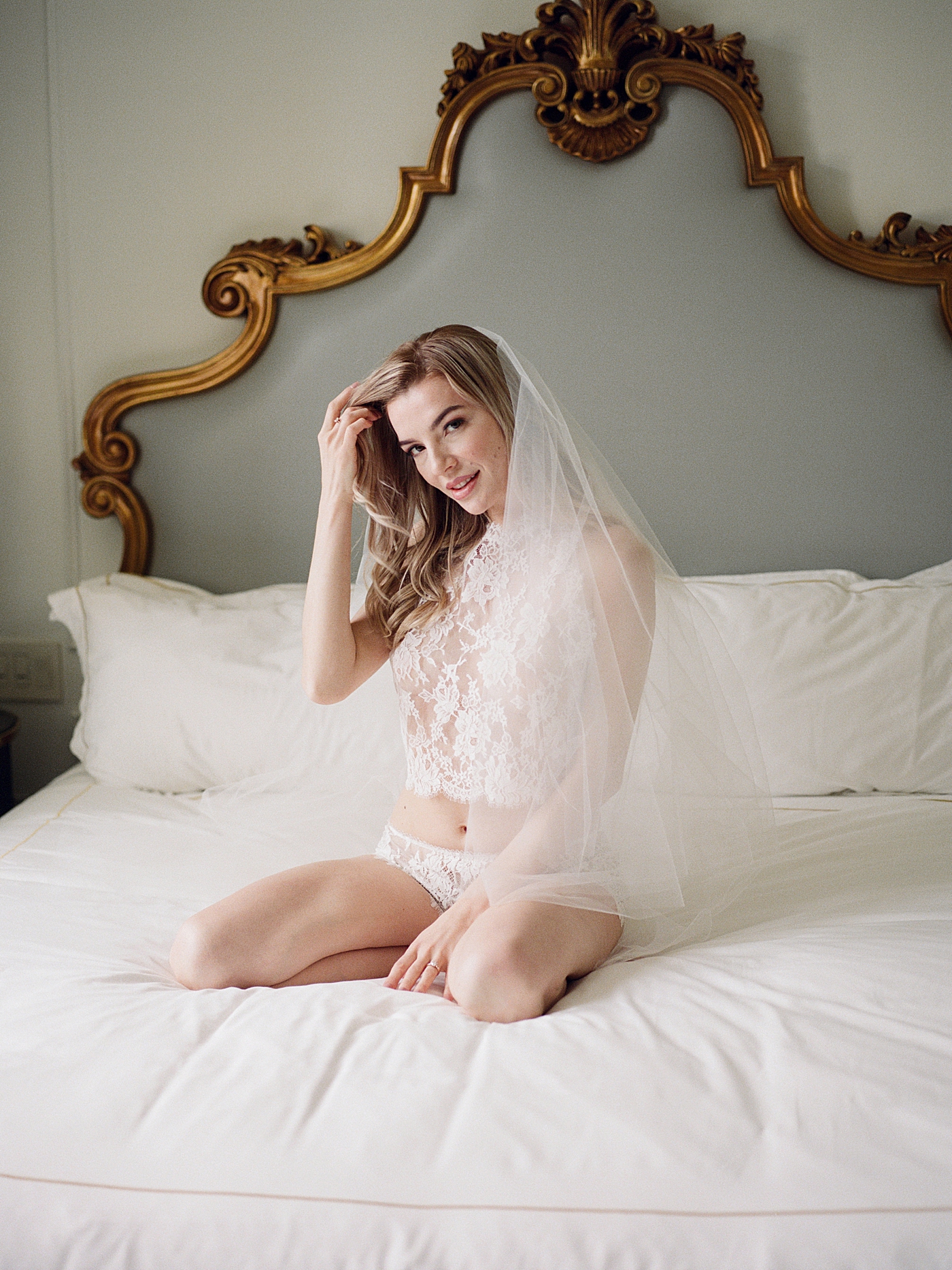 Bride-to-be smiling and posing in white lingerie on a romantic, luxe white bed | Image by Hope Helmuth Photography