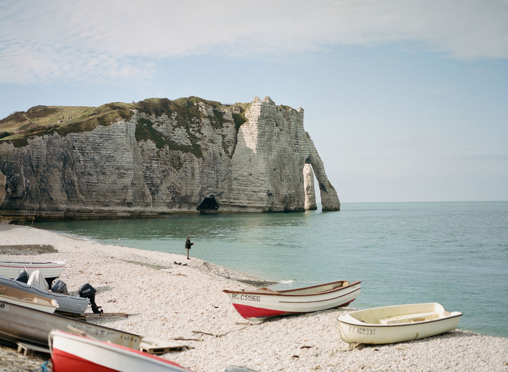 View of an empty French beach with cliffs in the back ground, calm water, and boats sitting on shore