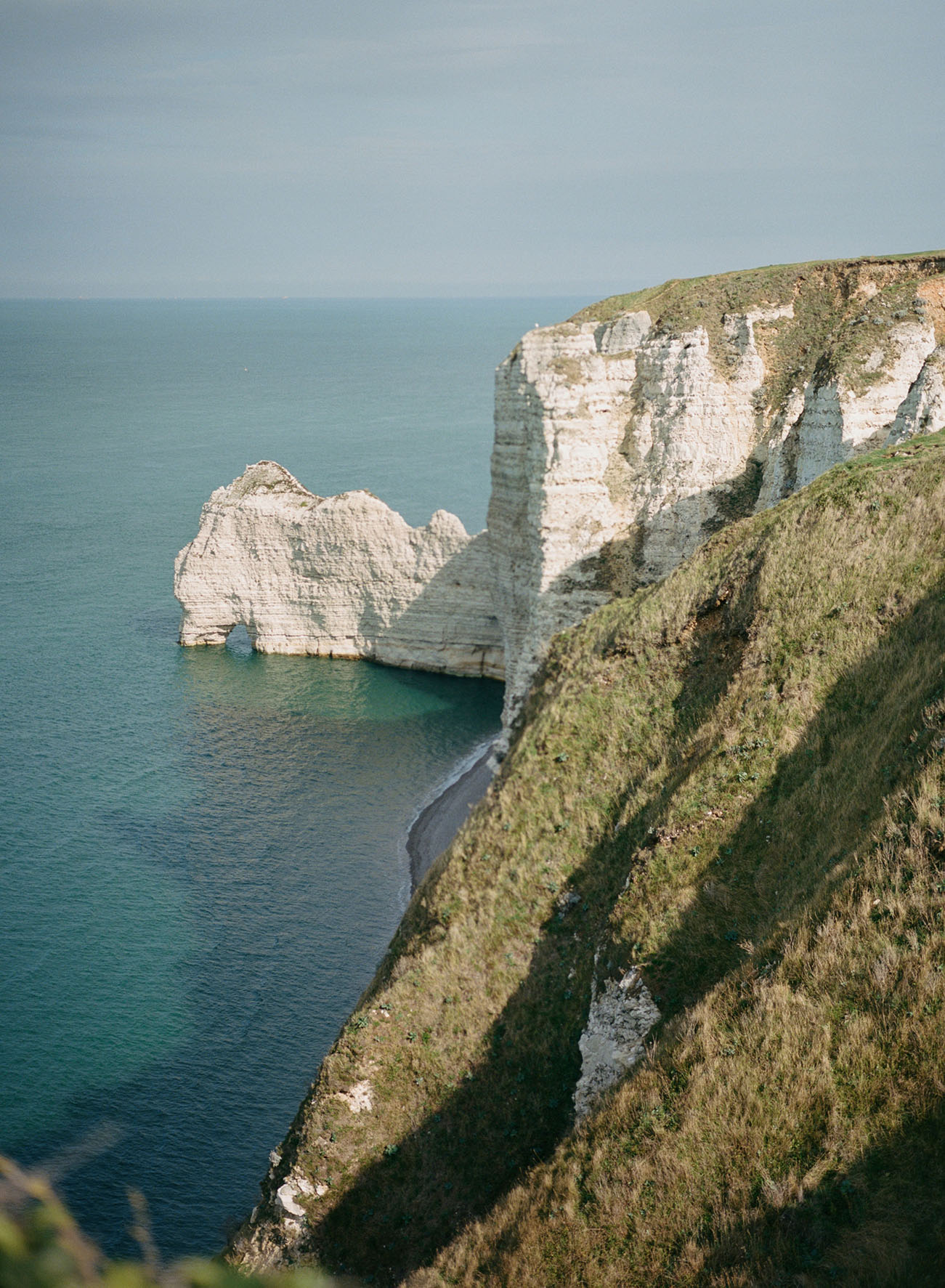 Large French cliffs on dropping down into a clear, calm blue ocean 