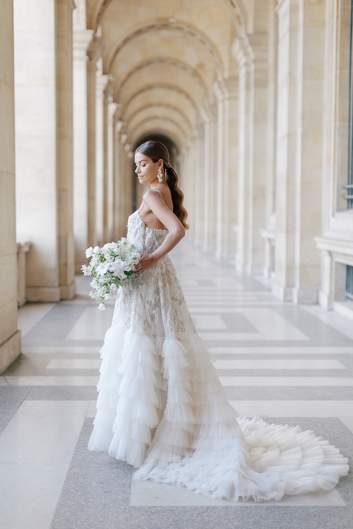 Bride standing in the outside hallway of the Louvre with a bouquet | Image by Hope Helmuth Photography