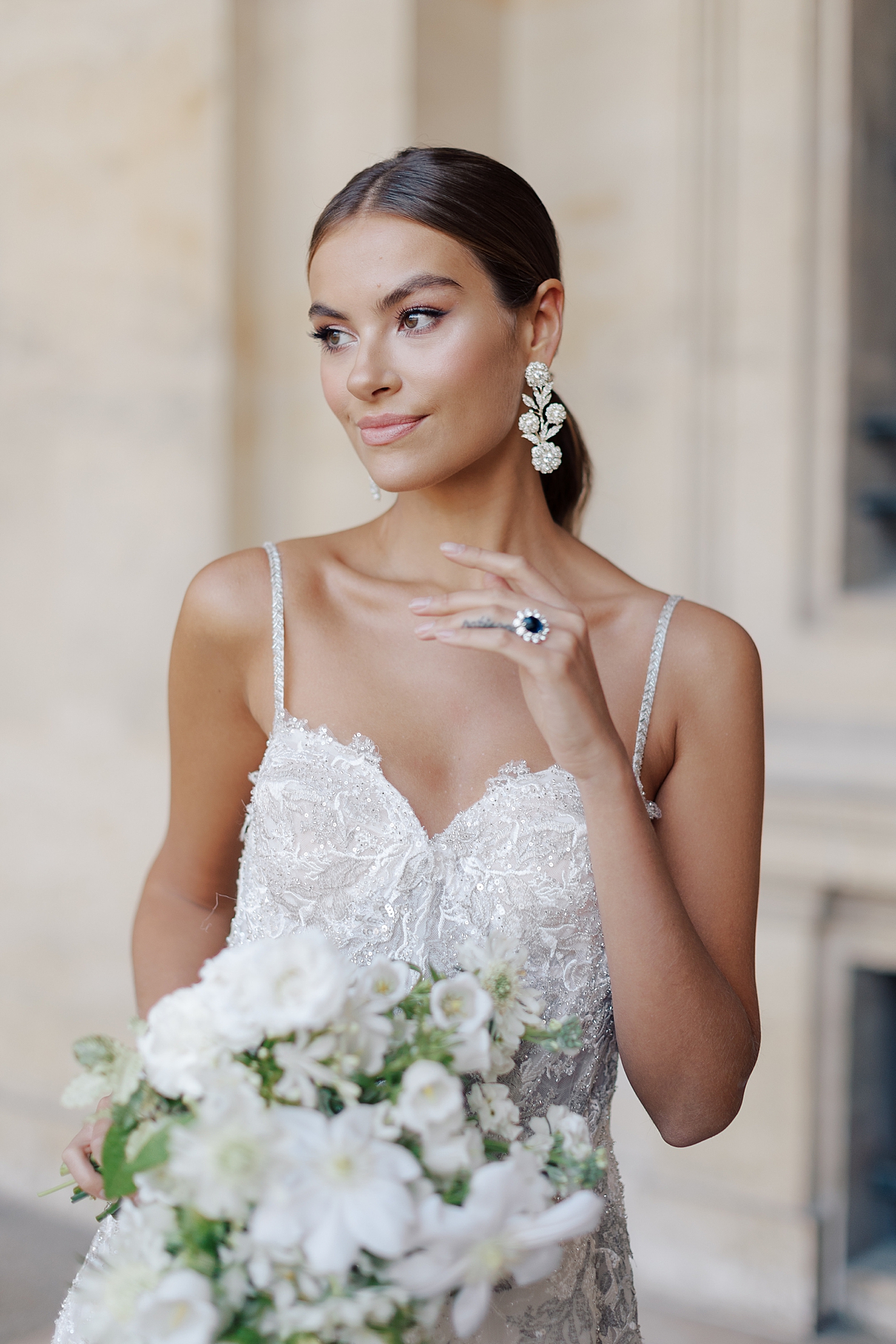 Close up of a bride standing in the outside hallway of the Louvre with a bouquet an engagement ring | Image by Hope Helmuth Photography