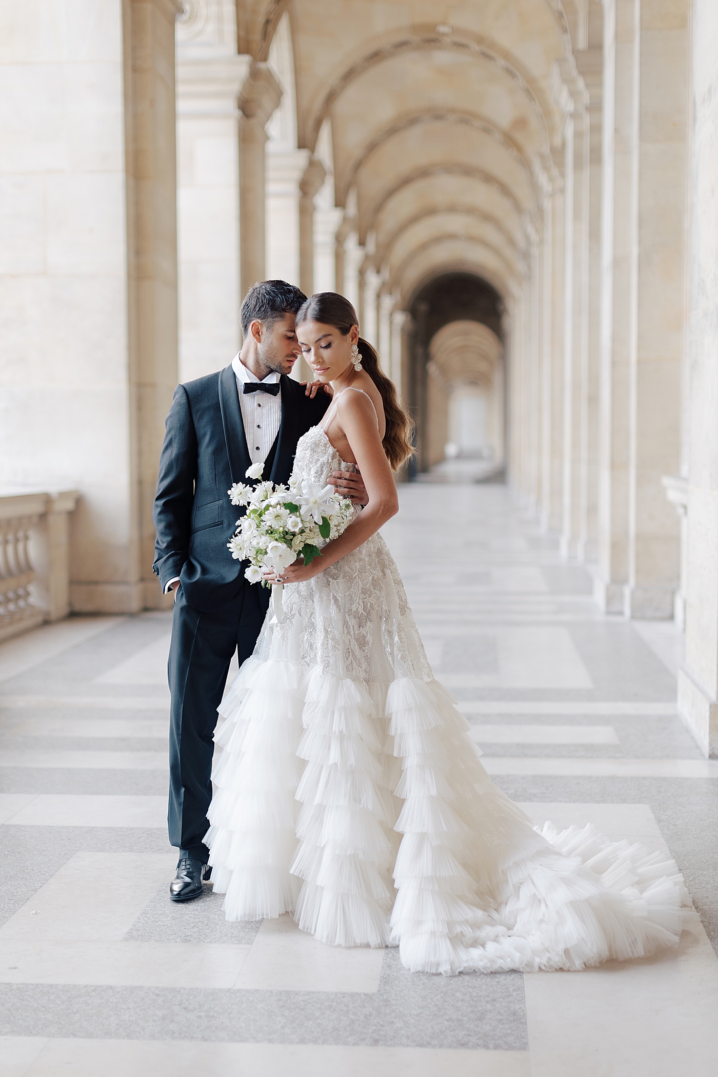 Bride and groom standing in the outside hallway of the Louvre with a bouquet and engagement ring | Image by Hope Helmuth Photography