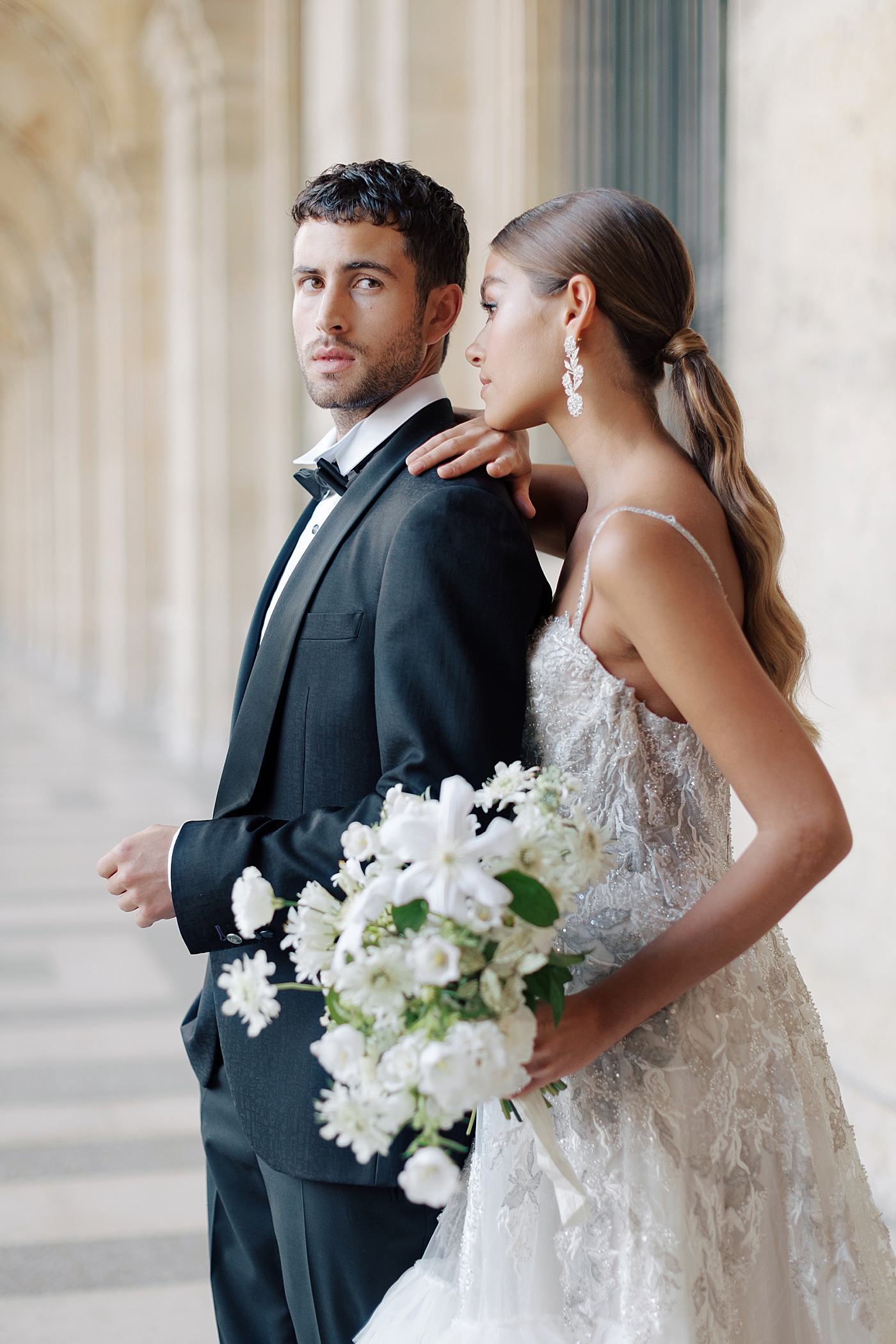 Close up of a bride and groom standing in the outside hallway of the Louvre with a bouquet | Image by Hope Helmuth Photography