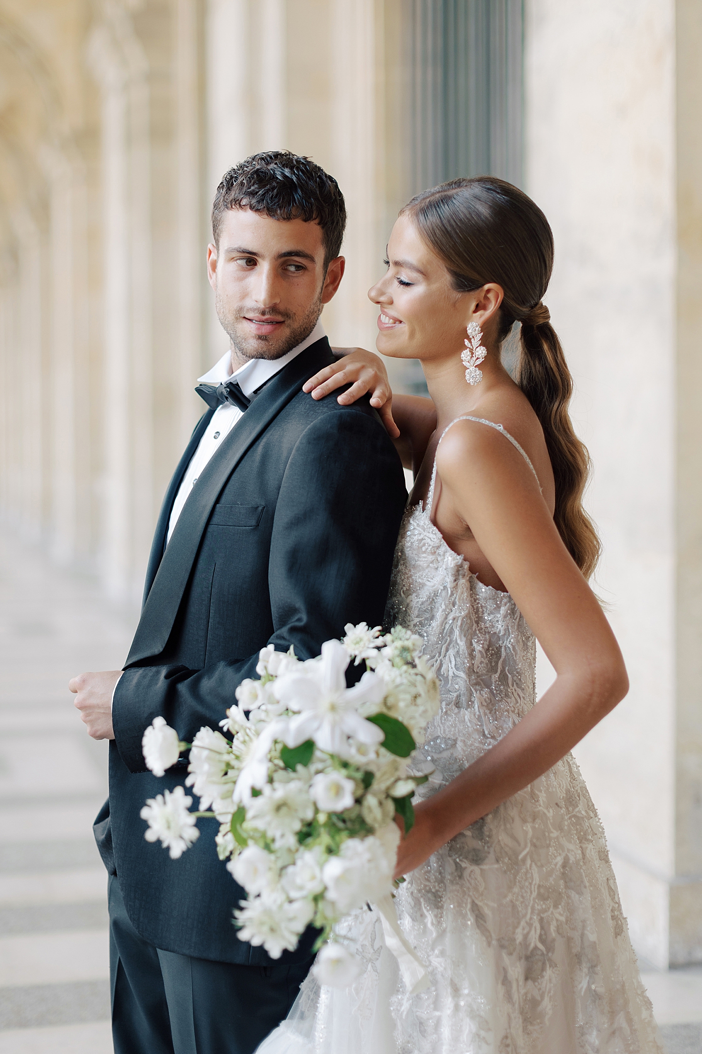 Bride and groom standing in the outside hallway of the Louvre with a bouquet | Image by Hope Helmuth Photography