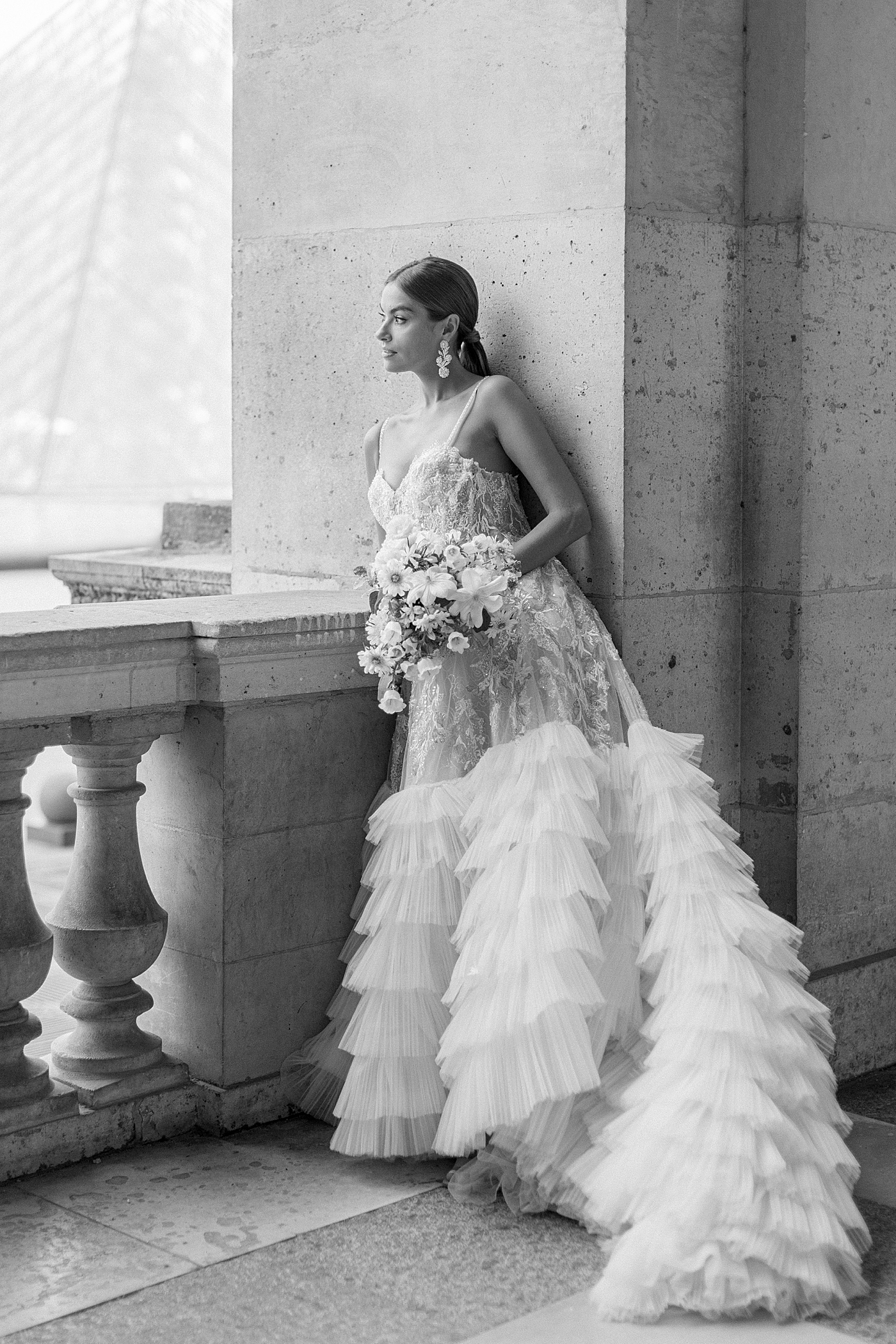 Black and white image of a bride in a wedding dress posing against a concrete pillar | Image by Hope Helmuth Photography